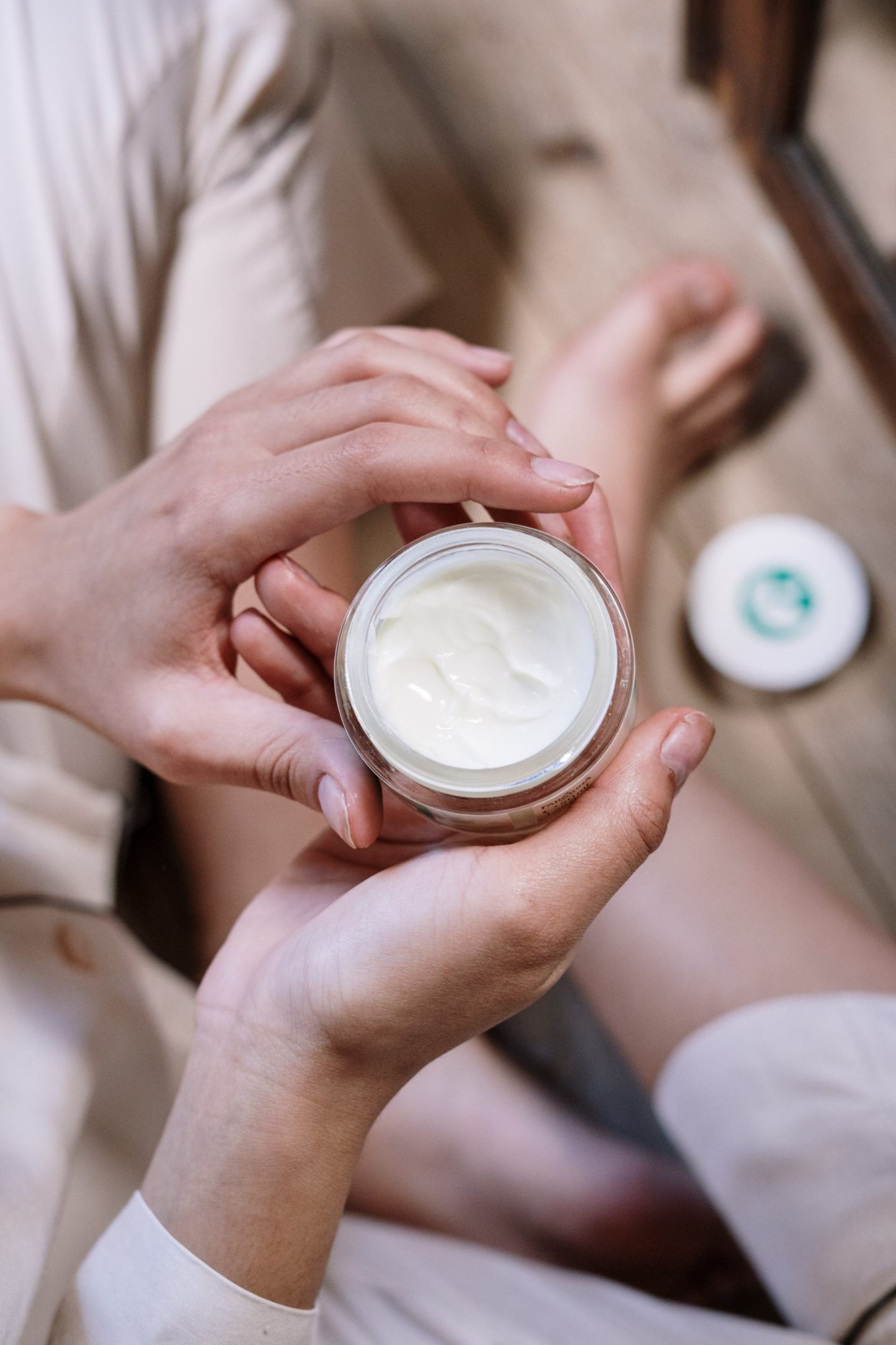 Woman looking at a pot of her skincare picks. The Skincare item is a pot of face cream.
